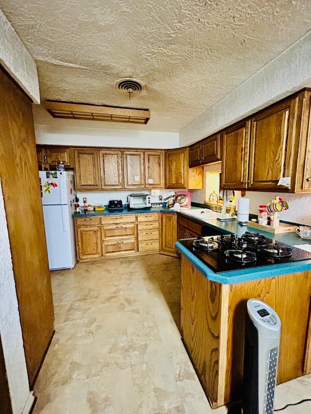 kitchen featuring visible vents, a sink, black gas cooktop, freestanding refrigerator, and brown cabinetry