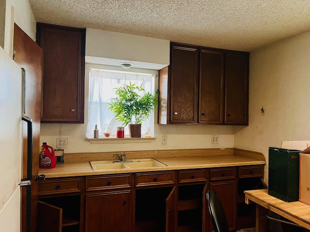 kitchen featuring a sink, a textured ceiling, freestanding refrigerator, dark brown cabinetry, and light countertops