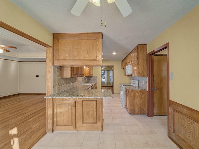 kitchen with sink, white appliances, ceiling fan, light stone countertops, and kitchen peninsula