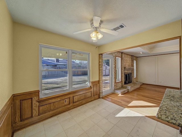 unfurnished living room featuring ceiling fan, a brick fireplace, and a textured ceiling