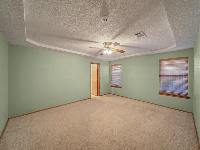 unfurnished room featuring a raised ceiling, light carpet, and a wealth of natural light