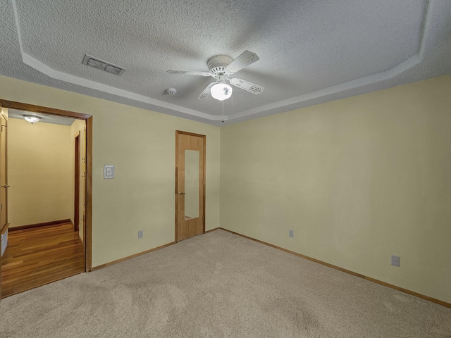 carpeted empty room featuring a raised ceiling, a textured ceiling, and ceiling fan