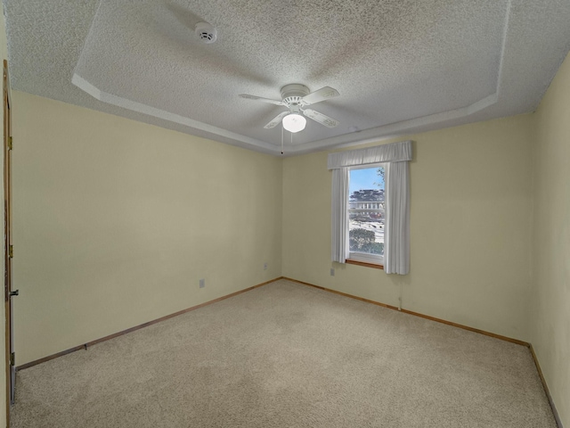 unfurnished room with ceiling fan, light colored carpet, a raised ceiling, and a textured ceiling