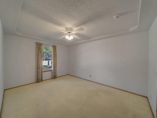 spare room with ceiling fan, a tray ceiling, and carpet flooring