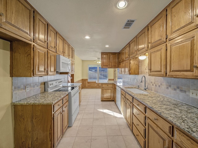 kitchen with sink, white appliances, light tile patterned floors, ceiling fan, and light stone countertops