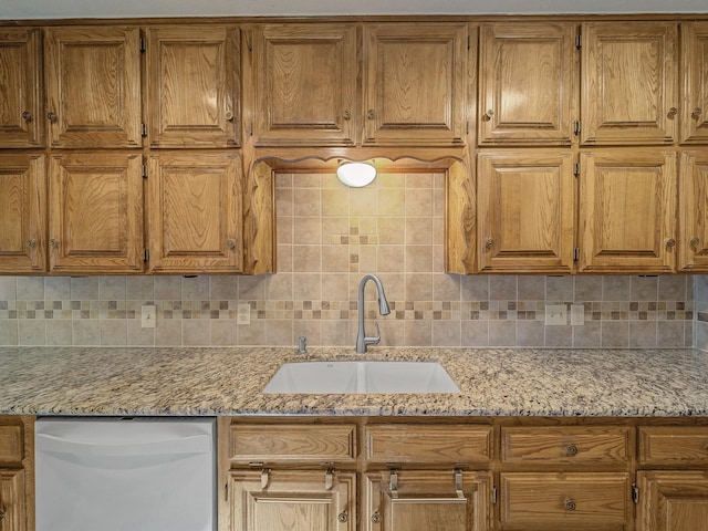 kitchen featuring light stone countertops, dishwasher, sink, and decorative backsplash