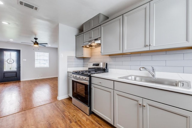 kitchen with gray cabinetry, stainless steel gas range oven, sink, ceiling fan, and decorative backsplash