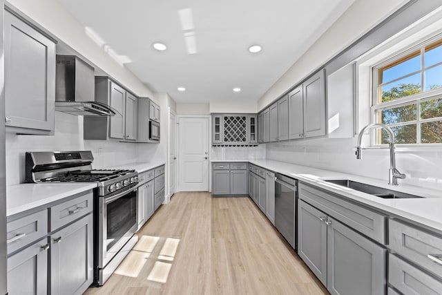 kitchen with sink, wall chimney exhaust hood, gray cabinets, appliances with stainless steel finishes, and light hardwood / wood-style floors