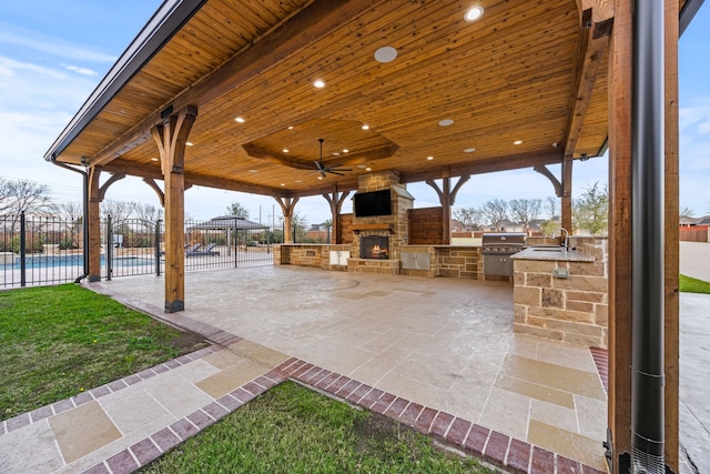 view of patio featuring ceiling fan, sink, exterior kitchen, a grill, and an outdoor stone fireplace