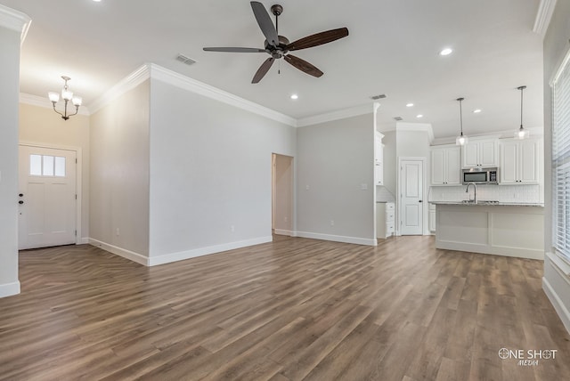 unfurnished living room with ceiling fan with notable chandelier, dark wood-type flooring, ornamental molding, and sink