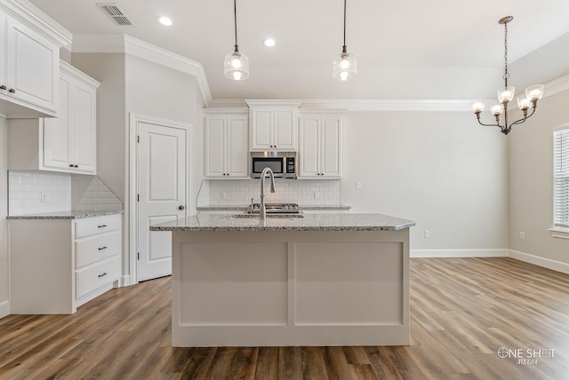 kitchen featuring white cabinets, light stone countertops, an island with sink, and hardwood / wood-style floors