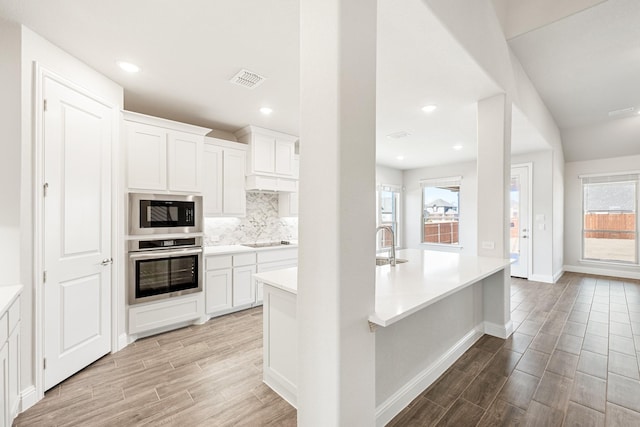 kitchen with white cabinetry, backsplash, black electric cooktop, built in microwave, and stainless steel oven