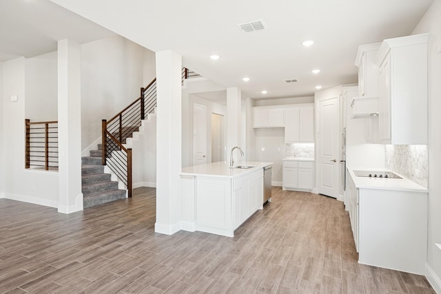 kitchen featuring white cabinetry, an island with sink, sink, black electric stovetop, and light wood-type flooring