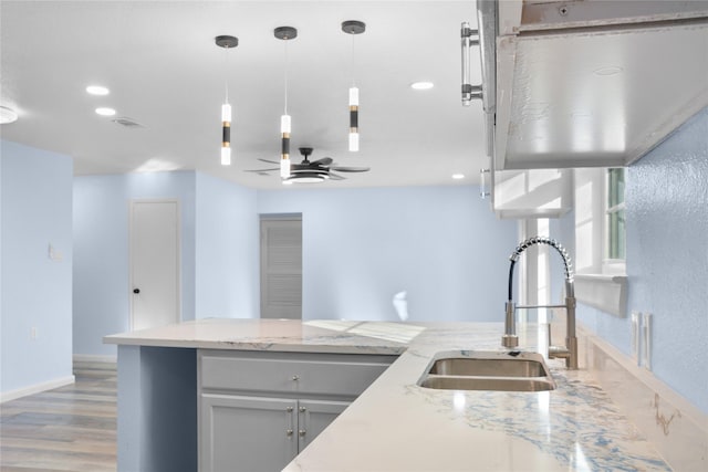 kitchen featuring sink, ceiling fan, light wood-type flooring, light stone countertops, and decorative light fixtures