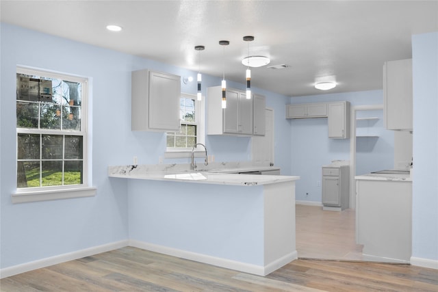 kitchen featuring kitchen peninsula, sink, pendant lighting, and light wood-type flooring