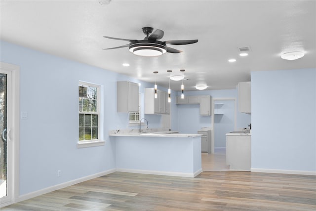 kitchen featuring kitchen peninsula, light wood-type flooring, ceiling fan, sink, and pendant lighting