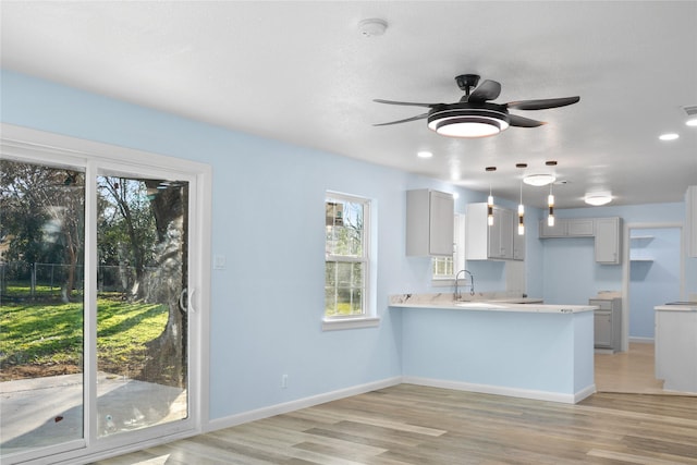 kitchen featuring ceiling fan, sink, hanging light fixtures, kitchen peninsula, and light wood-type flooring