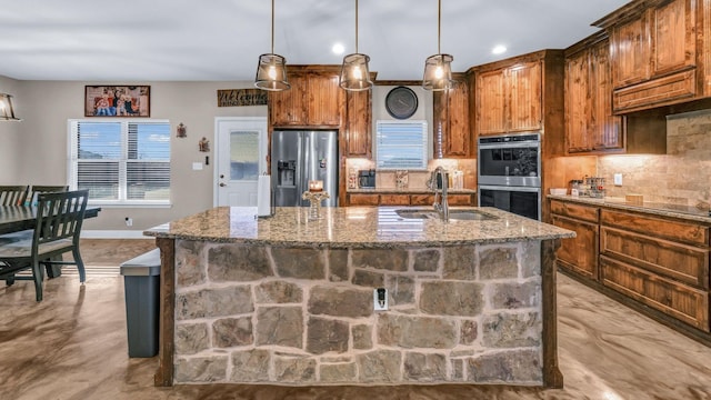 kitchen with stainless steel appliances, sink, hanging light fixtures, and an island with sink