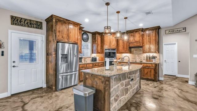 kitchen featuring light stone countertops, appliances with stainless steel finishes, decorative light fixtures, sink, and a kitchen island with sink