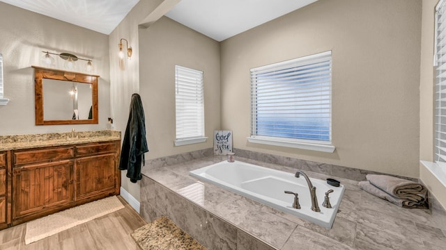 bathroom with a relaxing tiled tub, wood-type flooring, and vanity