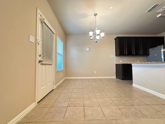 kitchen with tasteful backsplash, stainless steel refrigerator, light tile patterned floors, and a notable chandelier