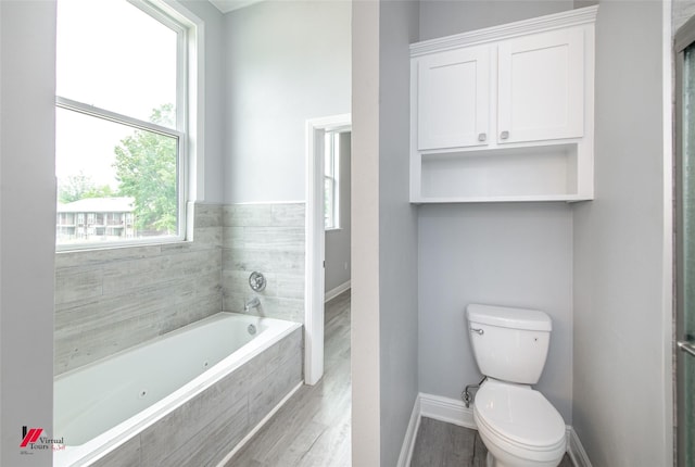 bathroom with hardwood / wood-style floors, tiled bath, and toilet