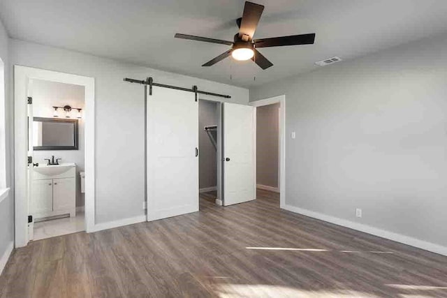 unfurnished bedroom with dark wood-type flooring, ensuite bathroom, sink, ceiling fan, and a barn door