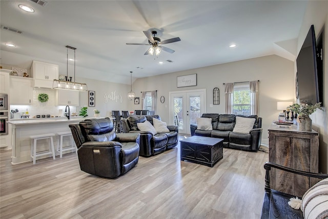 living room with ceiling fan, french doors, sink, lofted ceiling, and light wood-type flooring