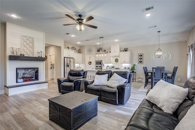 living room with sink, ceiling fan with notable chandelier, light hardwood / wood-style flooring, and a large fireplace