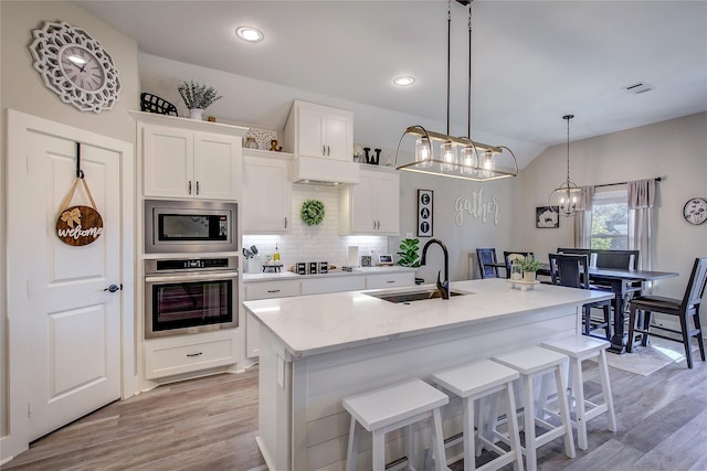 kitchen with a center island with sink, white cabinets, sink, tasteful backsplash, and stainless steel appliances