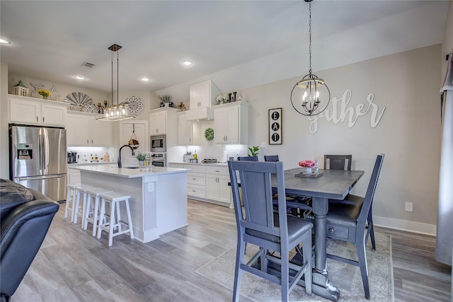 kitchen featuring appliances with stainless steel finishes, a center island with sink, white cabinets, and decorative light fixtures