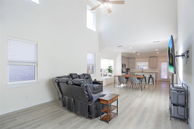 living room featuring a high ceiling, a healthy amount of sunlight, and light wood-type flooring