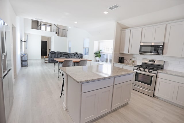 kitchen featuring a kitchen island, appliances with stainless steel finishes, white cabinetry, backsplash, and light hardwood / wood-style floors