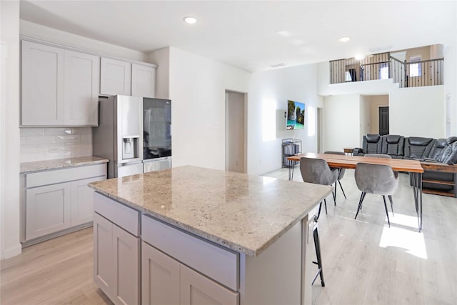 kitchen featuring light stone countertops, a center island, light hardwood / wood-style floors, and stainless steel fridge with ice dispenser