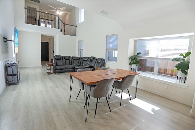 dining area featuring ceiling fan, a towering ceiling, and light hardwood / wood-style floors