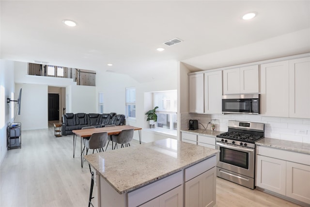 kitchen with lofted ceiling, stainless steel gas range oven, a center island, a kitchen breakfast bar, and white cabinets