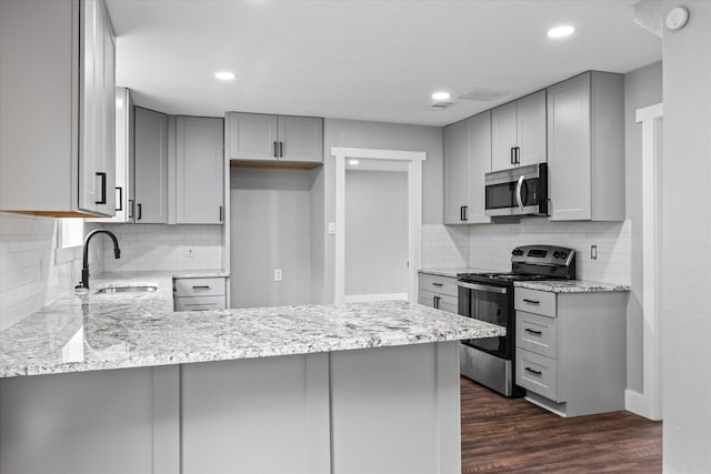 kitchen with sink, dark hardwood / wood-style flooring, kitchen peninsula, gray cabinets, and appliances with stainless steel finishes