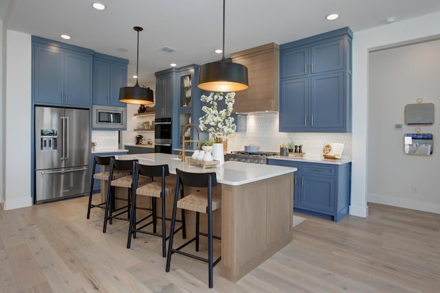 kitchen with appliances with stainless steel finishes, a breakfast bar, pendant lighting, an island with sink, and blue cabinetry