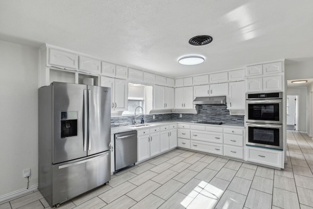 kitchen featuring appliances with stainless steel finishes, white cabinetry, sink, backsplash, and a textured ceiling