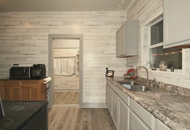 kitchen with wood walls, sink, black appliances, and light hardwood / wood-style flooring