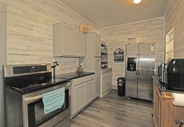 kitchen with gray cabinetry, wooden walls, dark hardwood / wood-style flooring, and stainless steel appliances