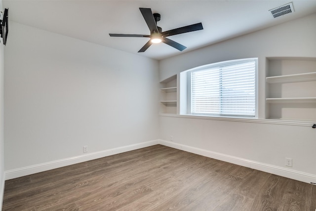 spare room featuring built in features, baseboards, a ceiling fan, visible vents, and wood finished floors