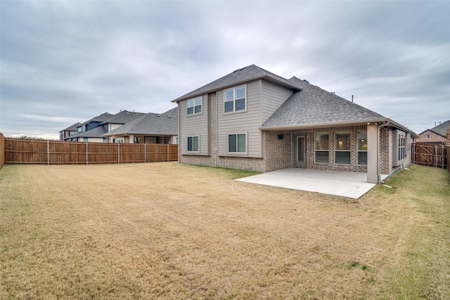 rear view of house featuring brick siding, a yard, a shingled roof, a patio area, and a fenced backyard