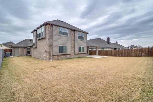 rear view of property featuring a yard, brick siding, a patio, and a fenced backyard