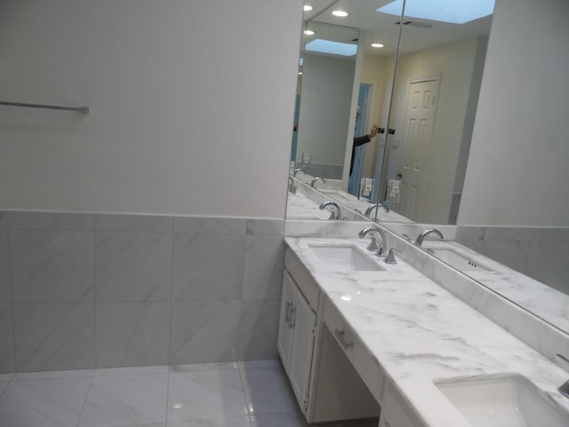 bathroom with tile patterned floors, vanity, tile walls, and a skylight