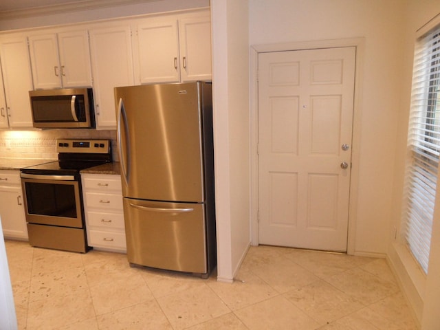 kitchen with tasteful backsplash, dark stone counters, stainless steel appliances, crown molding, and white cabinets