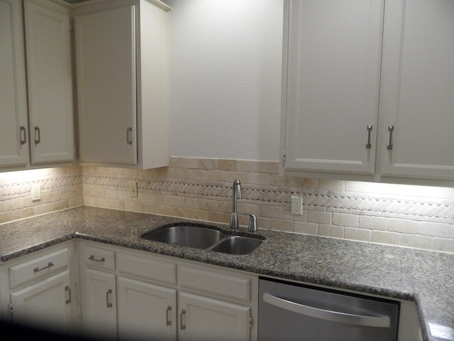 kitchen with sink, stainless steel dishwasher, backsplash, dark stone countertops, and white cabinets