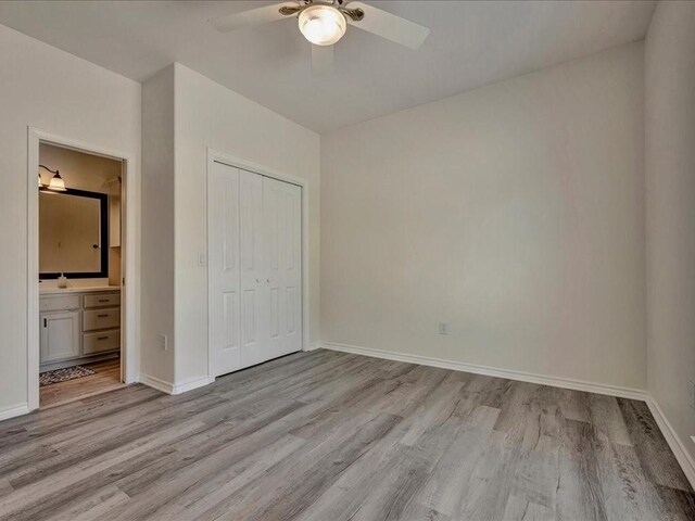 unfurnished bedroom featuring a closet, light wood-type flooring, ensuite bath, and baseboards