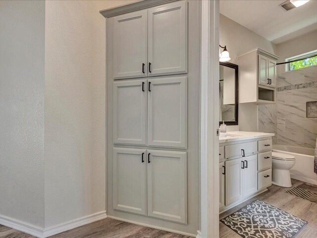 bathroom featuring toilet, wood finished floors, vanity, baseboards, and shower / bathing tub combination