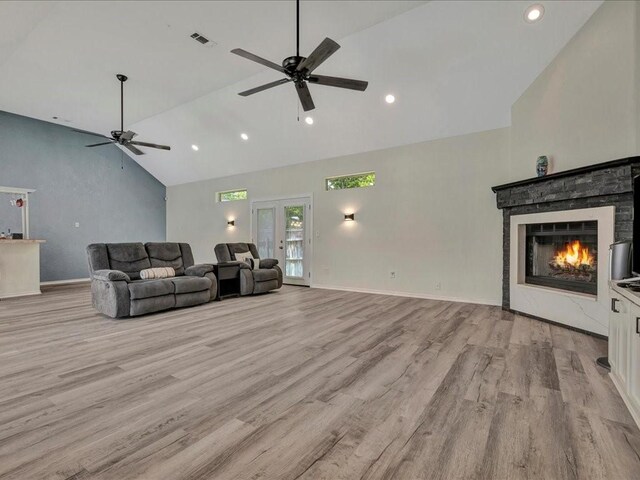 living room with high vaulted ceiling, a warm lit fireplace, light wood finished floors, and a ceiling fan